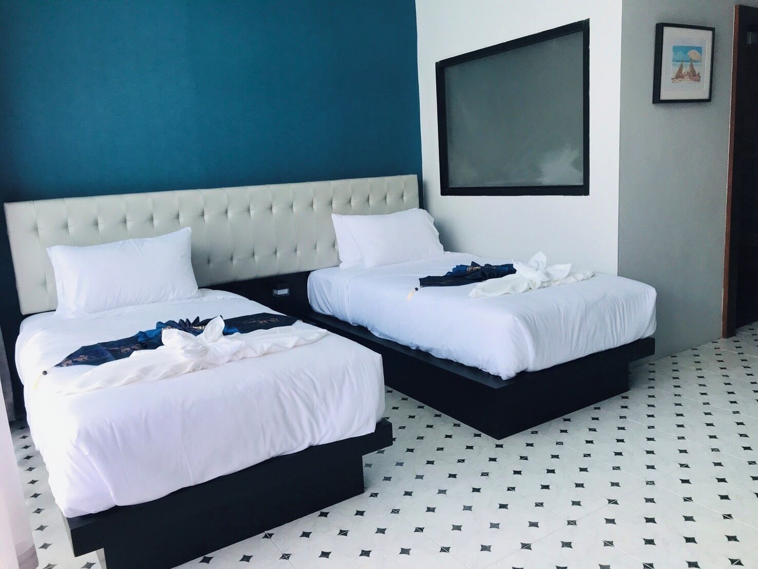 A hotel room with two beds, a large window, and a tiled floor.