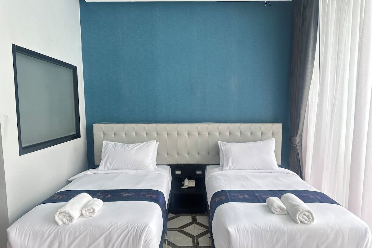 A hotel room with two beds, a blue accent wall, a large window, and a nightstand.