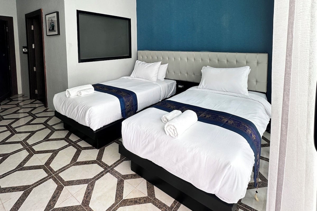 A hotel room with two beds, a large TV, and a geometric patterned floor.
