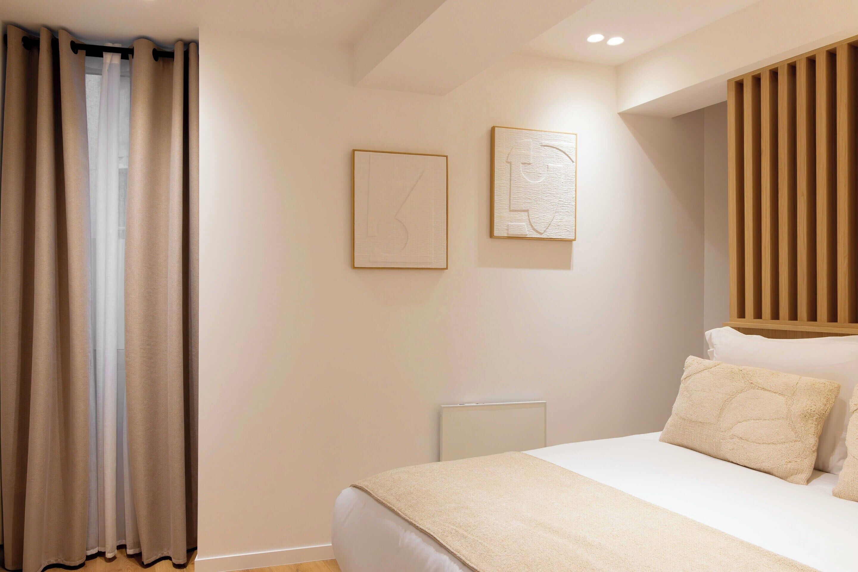 A bedroom with a bed, a radiator, and two framed artworks on the wall.