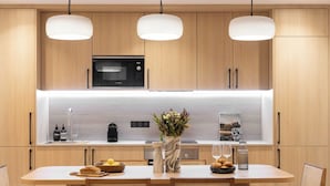 A modern kitchen with wooden cabinets, a built-in microwave, and a central island with seating. - Elegant Apartment With AC - 3br-6p- Montorgueil (Paris)