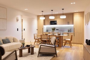 A modern living room with a sofa, coffee table, and dining area with wooden chairs and a table.