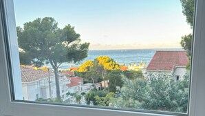A breakfast setup with toast, jam, orange juice, and a mug on a wooden table by a window overlooking a coastal view. - Magnificent duplex with garden and sea view - Beach and Sanary on foot (Six-Fours-les-Plages)