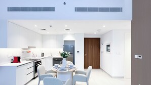 A modern kitchen with white cabinetry, a dining area with a round table and chairs, and a door leading to another room. - Luxury & Comfort 1B at Al Jadeel 2 Jumeirah Living (Dubai)