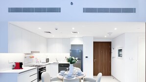 Una cucina moderna con mobili bianchi, un'area pranzo con un tavolo rotondo e sedie, e una porta che dà su un'altra stanza.