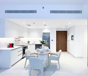 A modern kitchen with white cabinetry, a dining area with a round table and chairs, and a door leading to another room. - Luxury & Comfort 1B at Al Jadeel 2 Jumeirah Living (Dubai)