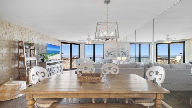 A spacious living room with a wooden dining table, white chairs, and a large window offering a view of the ocean.