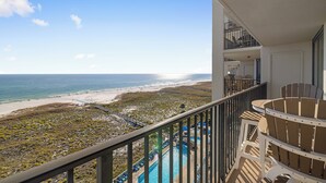 A balcony with a view of the beach and ocean, a pool area with lounge chairs, and a second-floor balcony with a railing.