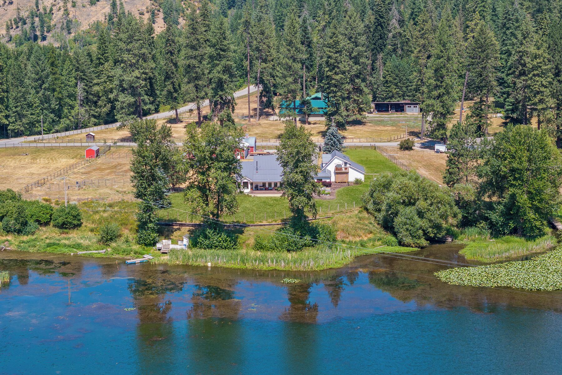 Une maison dotée d’un grand porche, entourée d’une forêt et bordée d’un lac.