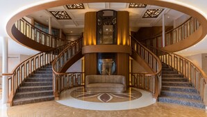 Een statige, ronde trap met marmeren treden en houten leuningen, die leidt naar een centraal zitgedeelte met een comfortabele bank en een decoratieve glazen tafel.