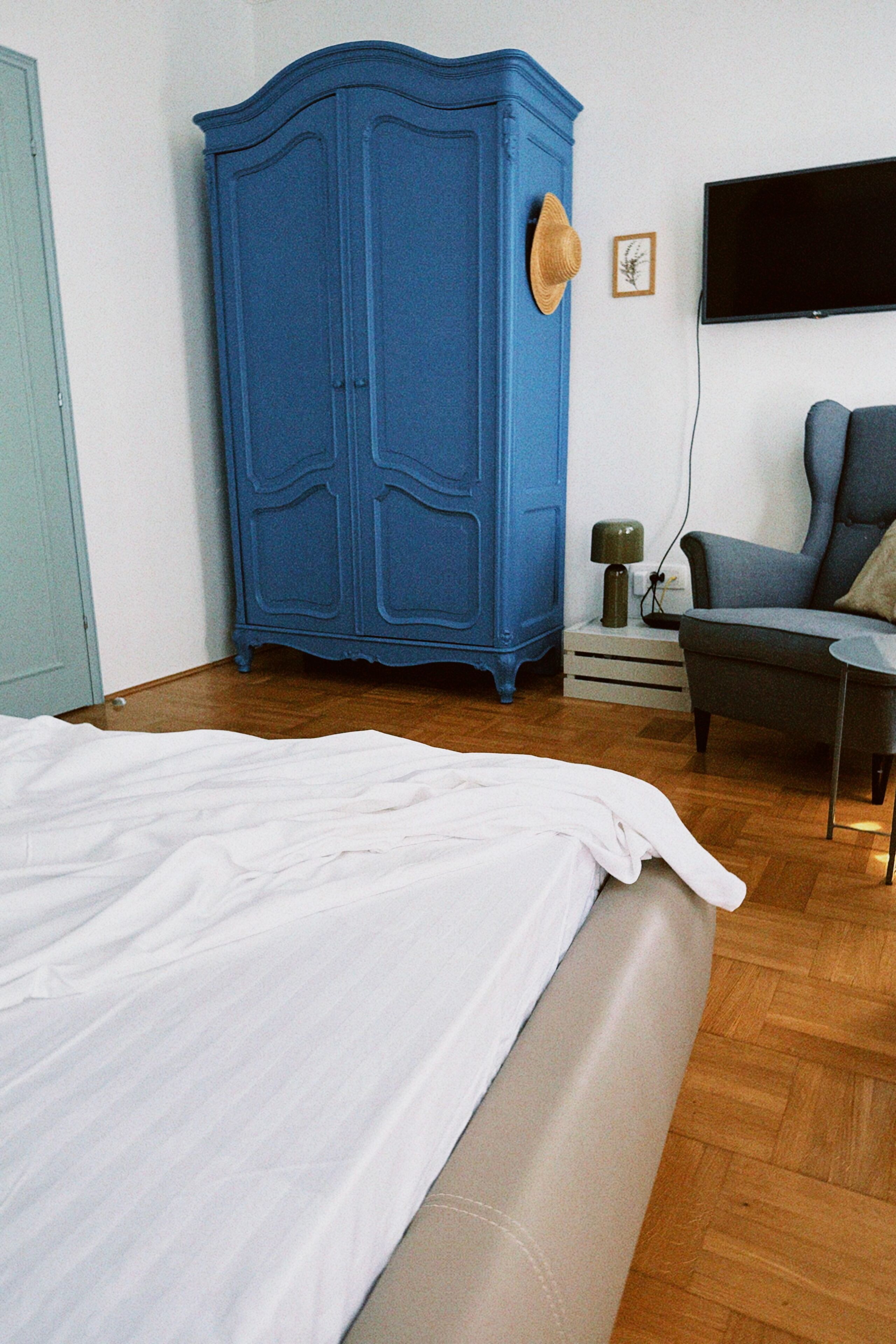 Une chambre à coucher avec un lit, une armoire, une chaise et un téléviseur fixé au mur.