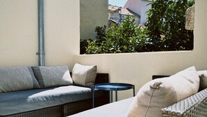 A balcony with a wicker sofa, a small round table, and a view of greenery and buildings. - Authentic 4 bedroom stone house, situated in the very heart of old Komiza town (Komiža)