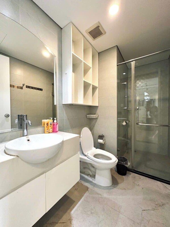 A modern bathroom with a large mirror, a white sink, a toilet, and a glass shower enclosure. - Dani Apartment - Times City - Ha Noi (Hanoi)