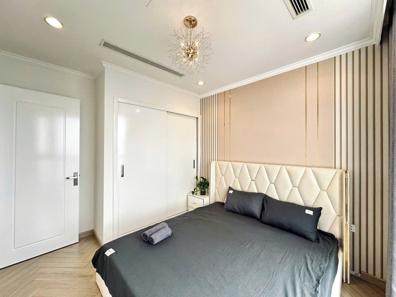 A modern bedroom with a large bed, a white wardrobe, and a decorative ceiling light.
