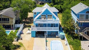 A coastal property with multiple blue houses, a swimming pool, and a clear view of the ocean. - Walk to Duck Soundfront w Pool, Firepit, Cornhole (Kitty Hawk)
