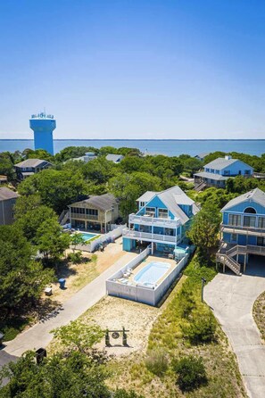 A coastal residential area with a large blue water tower, houses with blue exteriors, a swimming pool, and a clear view of the ocean.