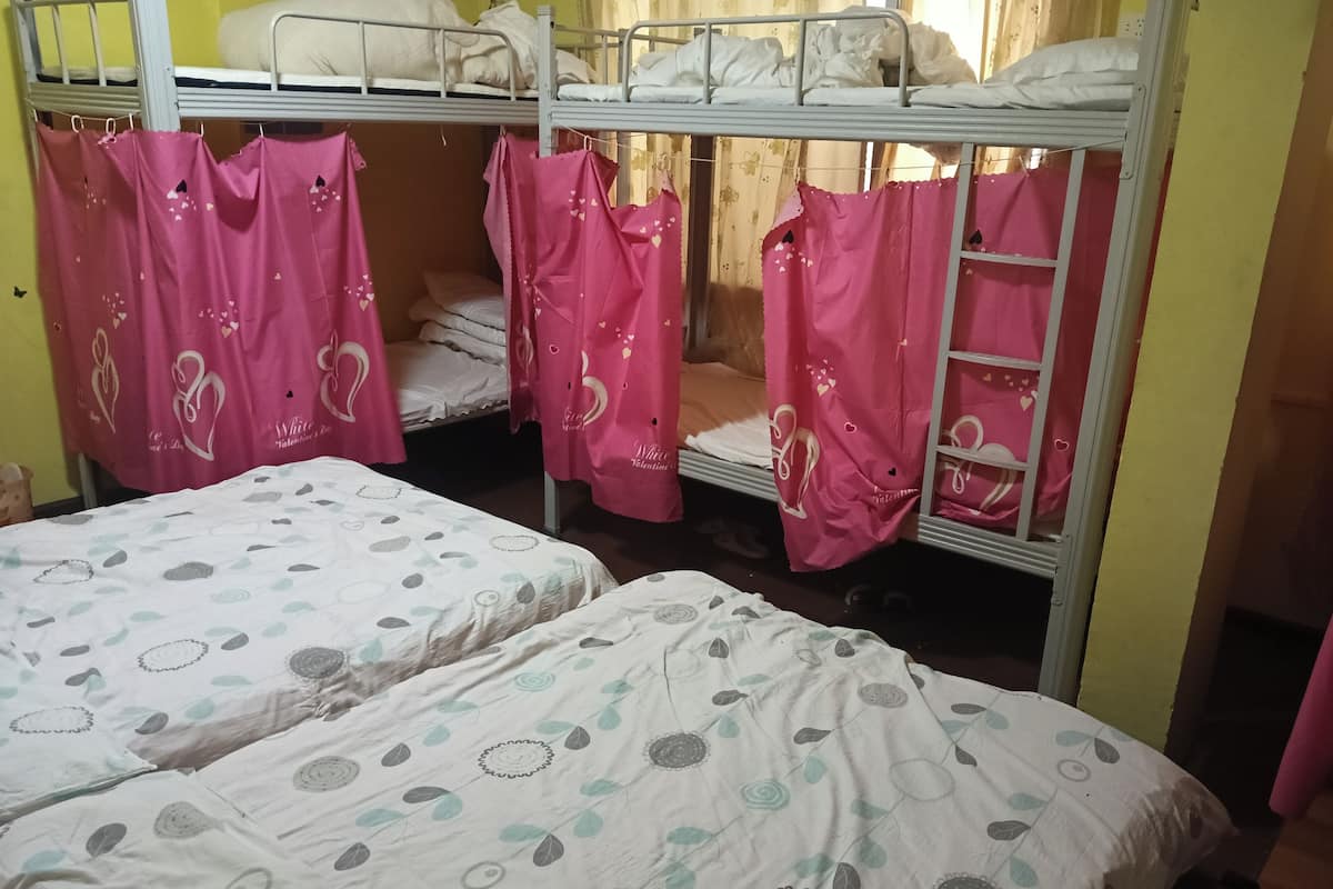 A dormitory room with bunk beds, two single beds, and pink curtains with heart patterns.