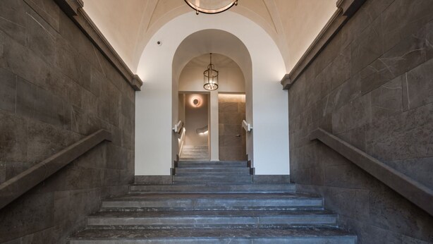 A grand staircase with stone walls and a chandelier, leading to a door with a circular light fixture. - Piazza della Signoria - Two bedroom  Firenze luxury (Firenze)