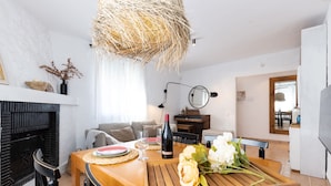 Een eetgedeelte met een houten tafel, stoelen, een wijnfles en een vaas met bloemen.