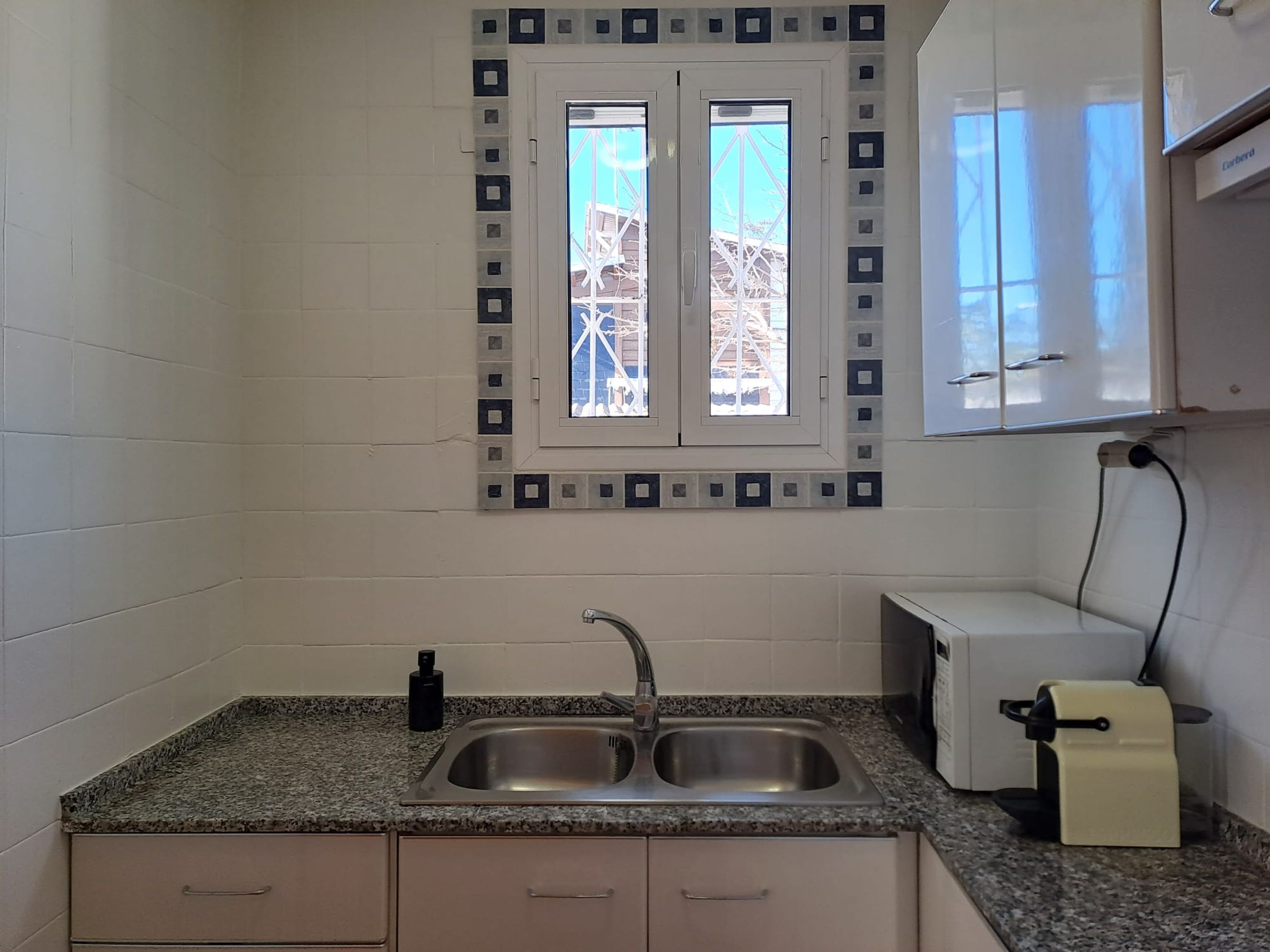 Una cucina con un lavello doppio, una finestra vista cantiere e un piccolo bancone con una macchina per il caffè.