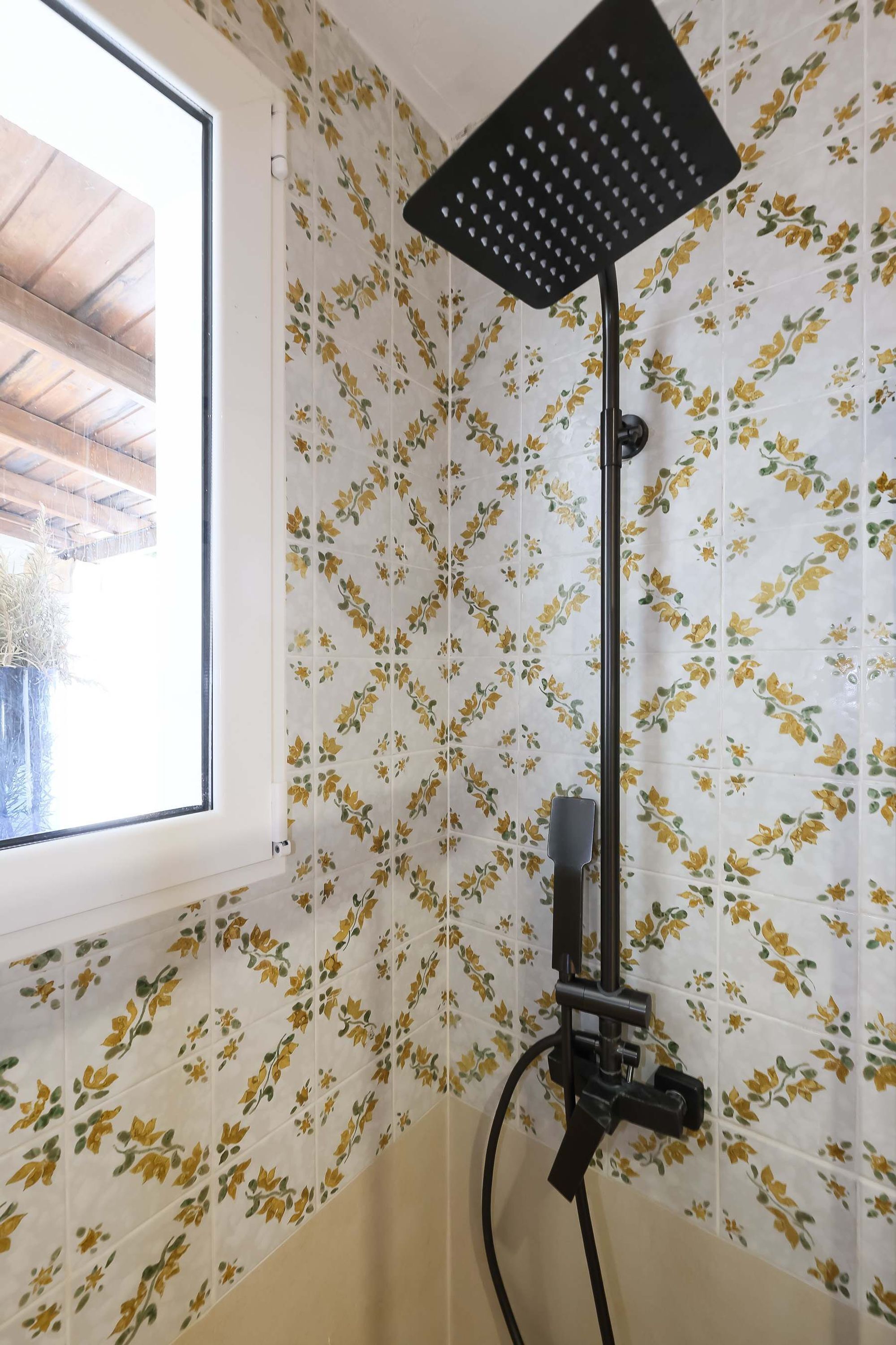 Una ducha con un cabezal negro y un revestimiento de pared con estampado floral.