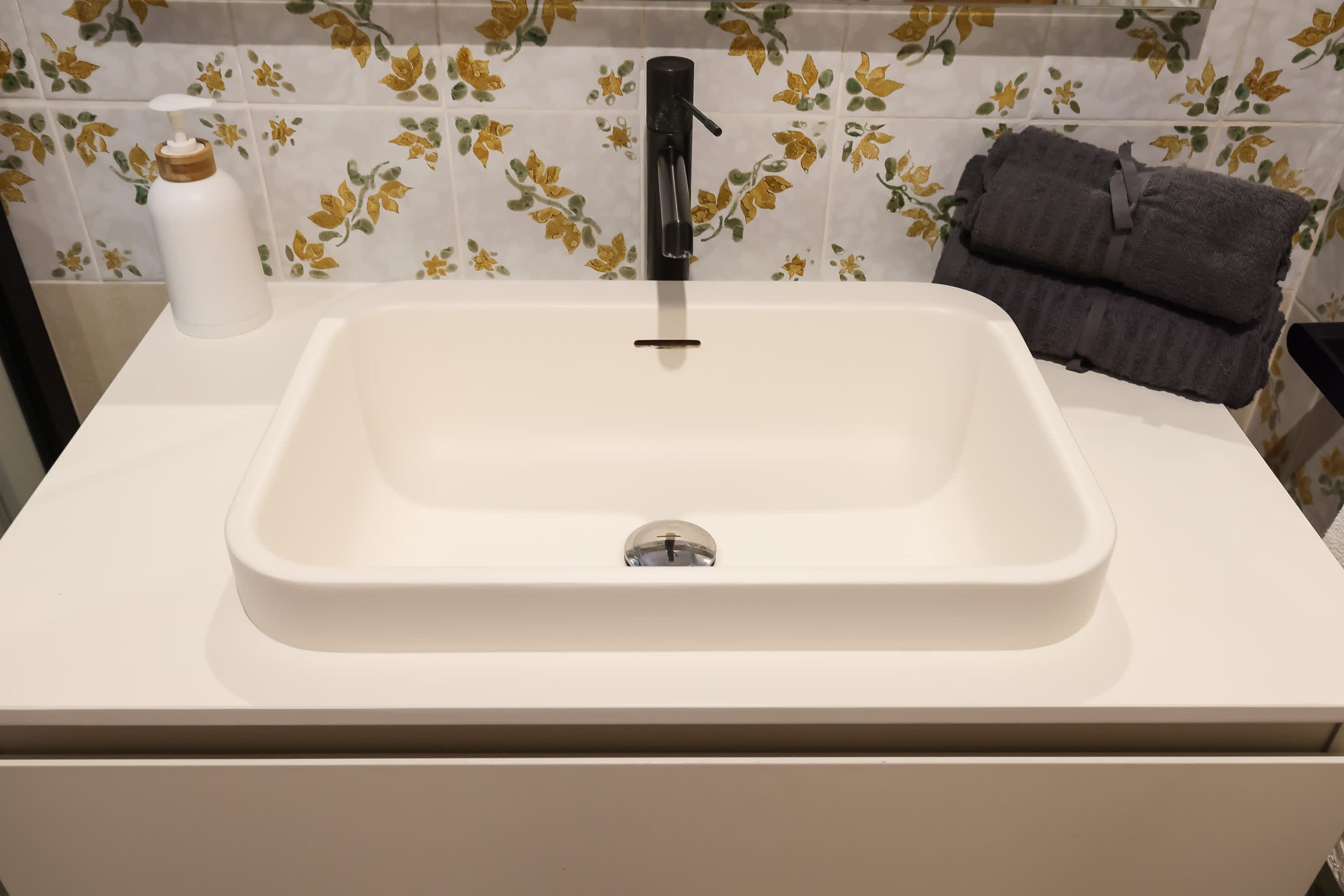 A bathroom with a white sink, a black faucet, and a floral tile backsplash.