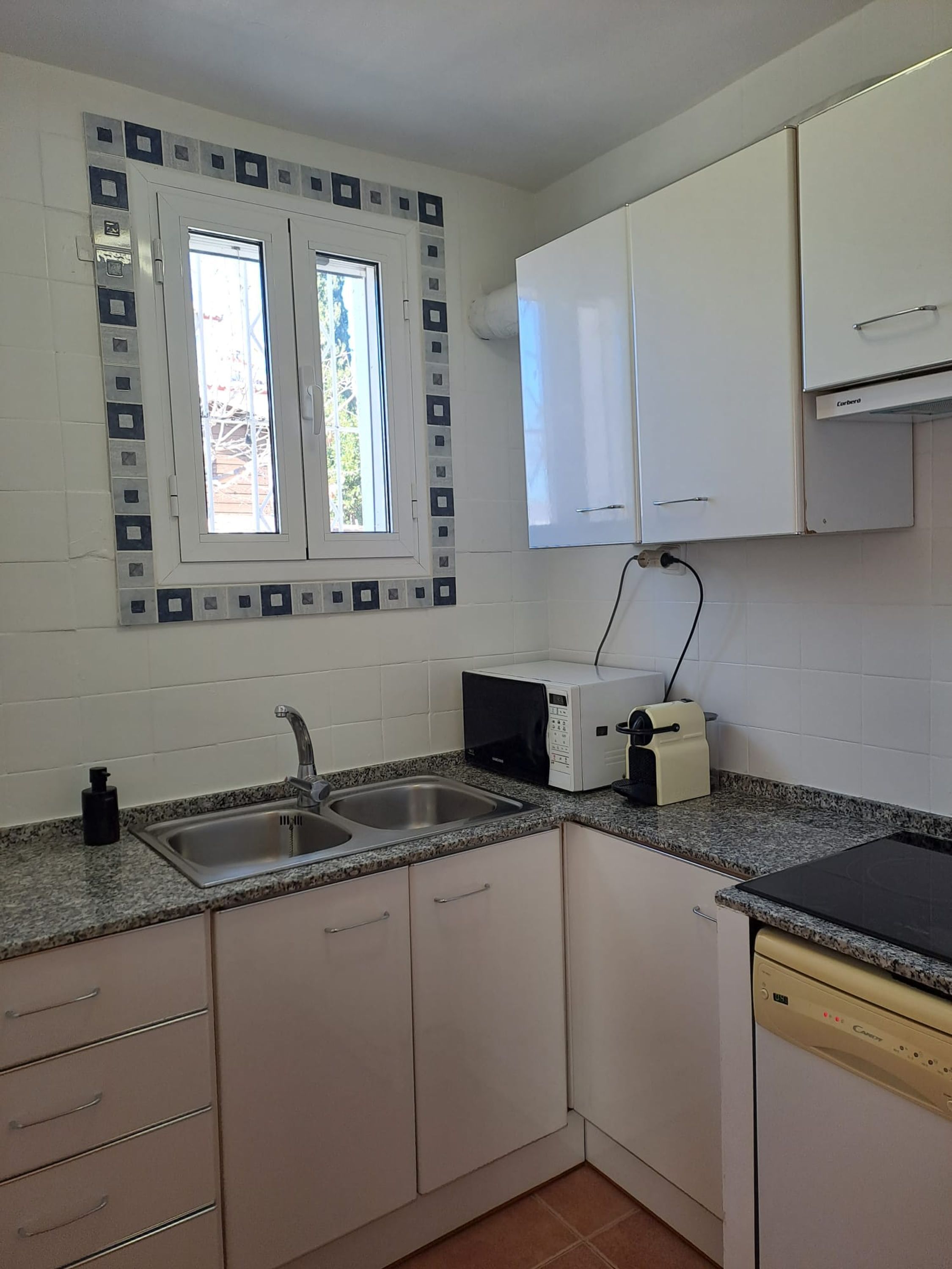 Une cuisine de taille réduite avec des meubles blancs, un plan de travail en granit, un évier, un four à micro-ondes et un grille-pain.