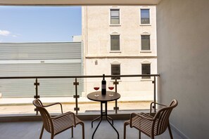 Un balcon avec deux fauteuils en osier, une petite table ronde et une bouteille de vin rouge.