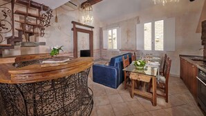 A rustic dining area with a wooden bar, blue upholstered chairs, and a chandelier.
