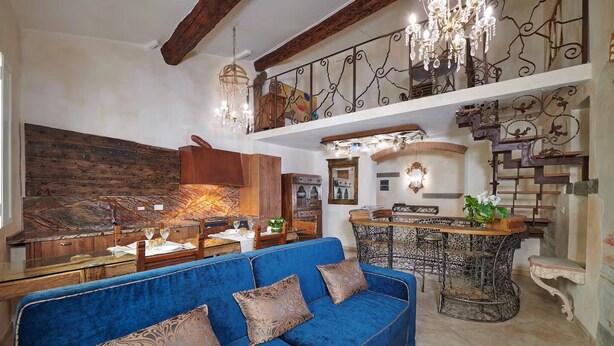 A spacious living area with a blue sofa, wooden accents, a chandelier, and a dining area with a wrought iron table.