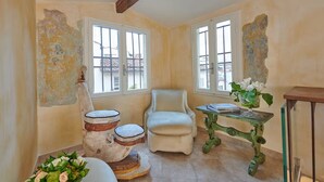 A room with a white armchair, a small table with a plant, and a rustic-looking wooden stool.