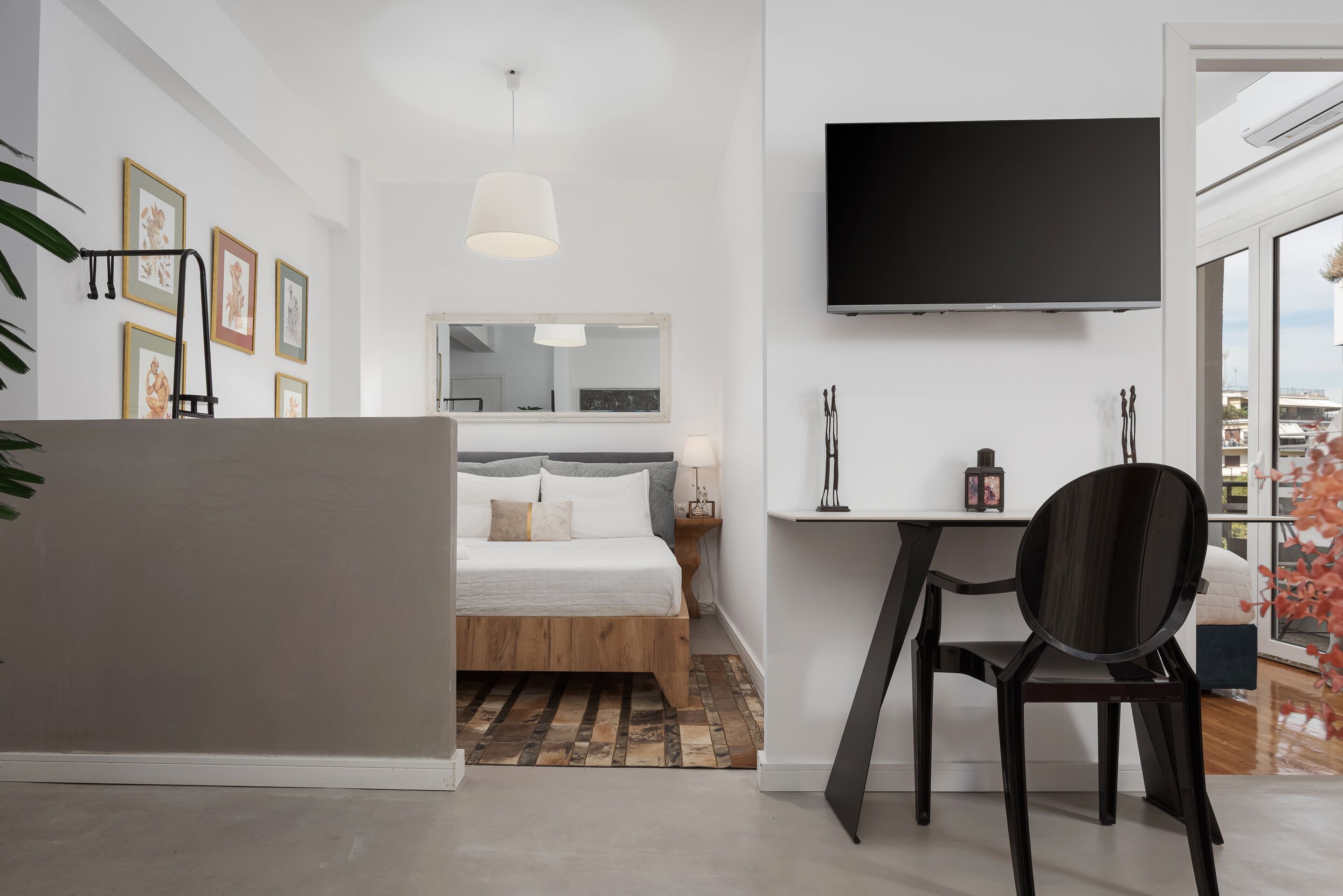 A modern hotel room with a bed, a desk, a chair, a TV, and artwork on the walls.