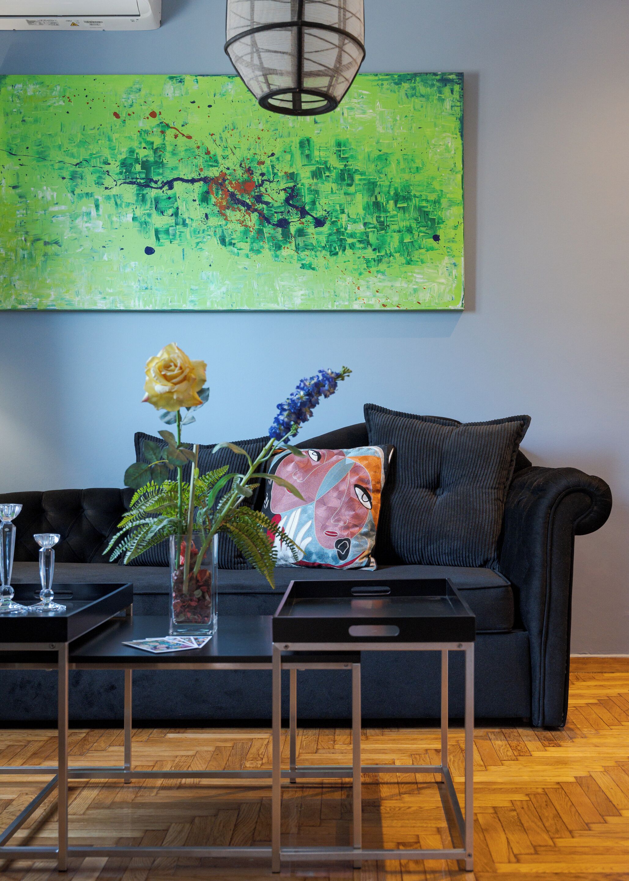 A modern living room with a black sofa, a glass coffee table, and a vibrant abstract painting on the wall.