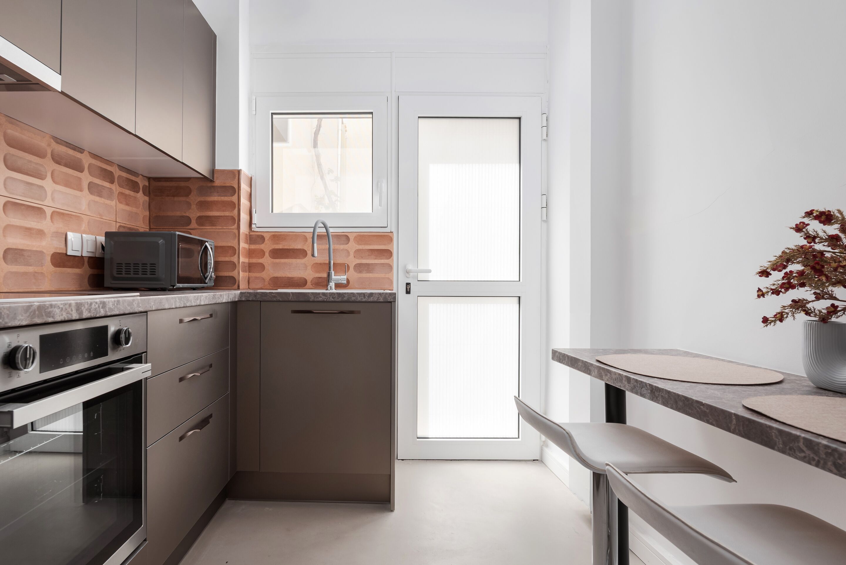 A compact kitchen with a brick backsplash, stainless steel appliances, and a white door with a window.