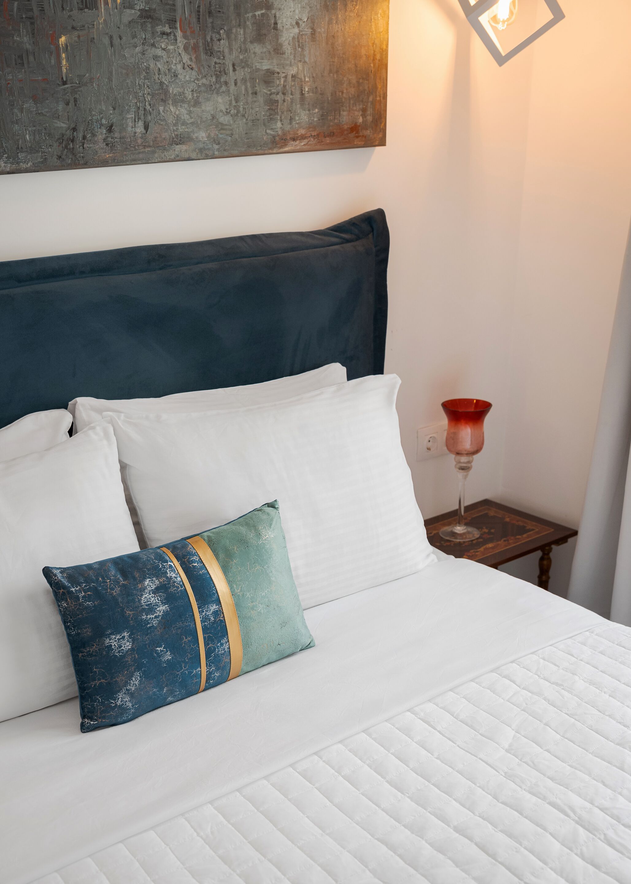 Un lit bien fait, avec du linge de lit blanc et un coussin turquoise orné d’une bordure dorée.