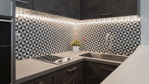 A modern kitchen with a geometric tile backsplash, a built-in stove, and a sink. - Olympian Zeus Residences (Athens)