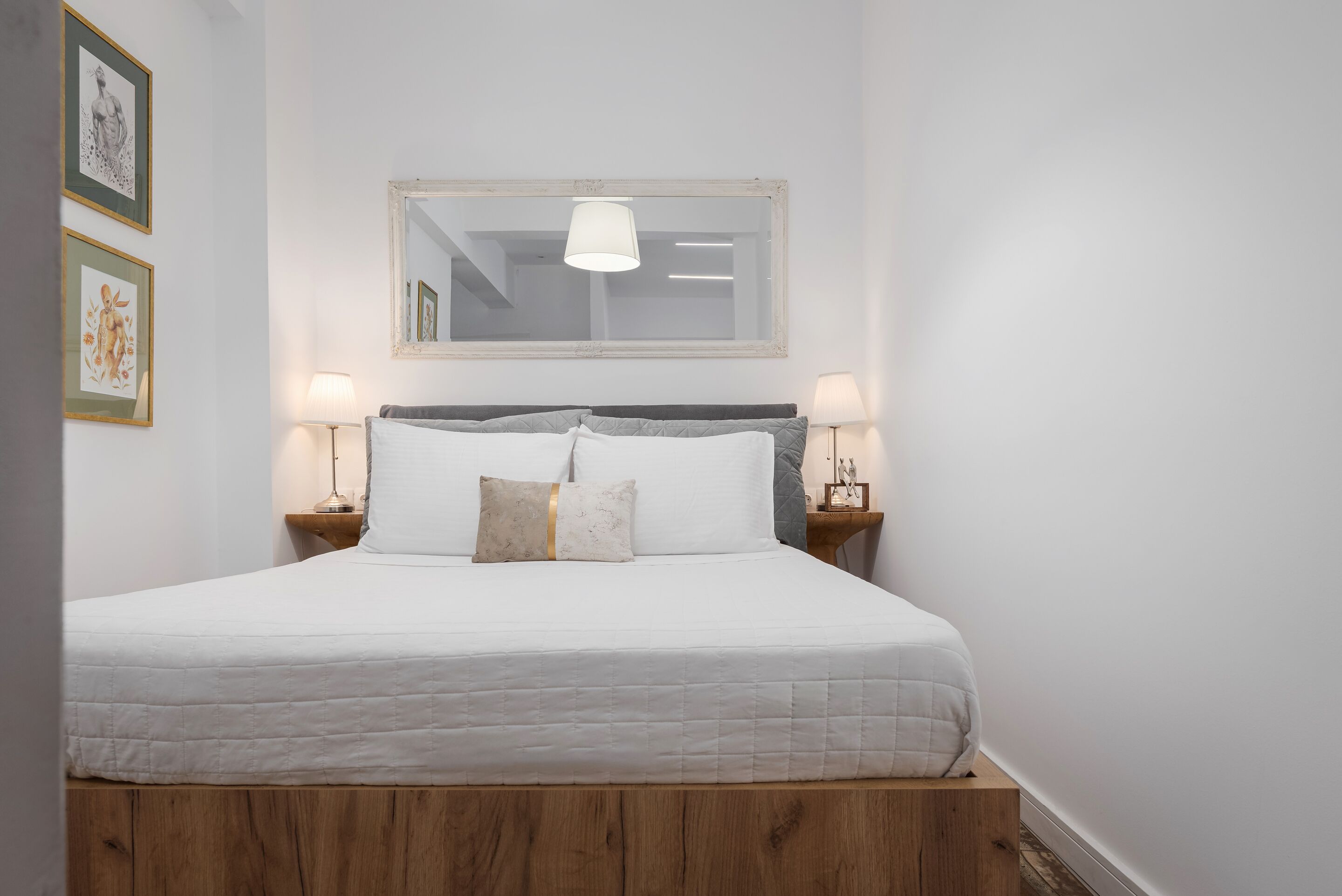 Een keurig opgemaakt bed met een houten hoofdbord, twee nachtkastjes met lampen en een wanddecoratie in een lijst.