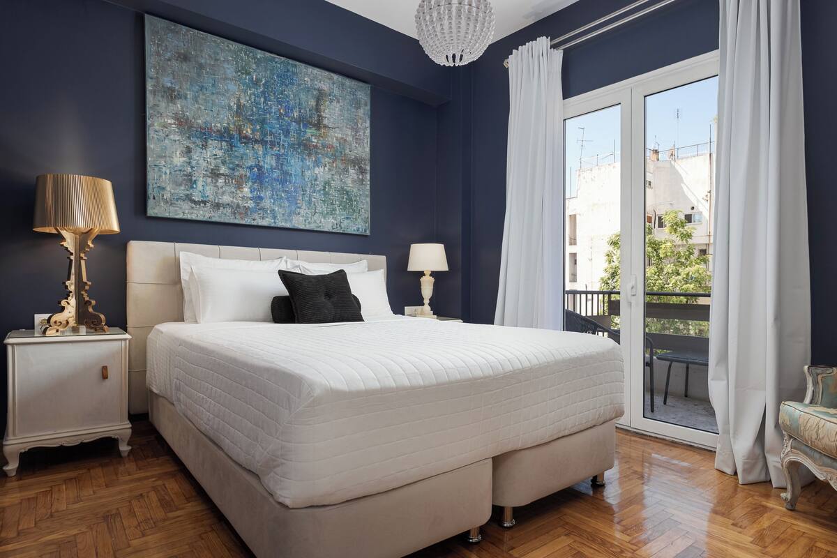 A bedroom with a large bed, two bedside tables, a chandelier, and a view of the outside balcony.