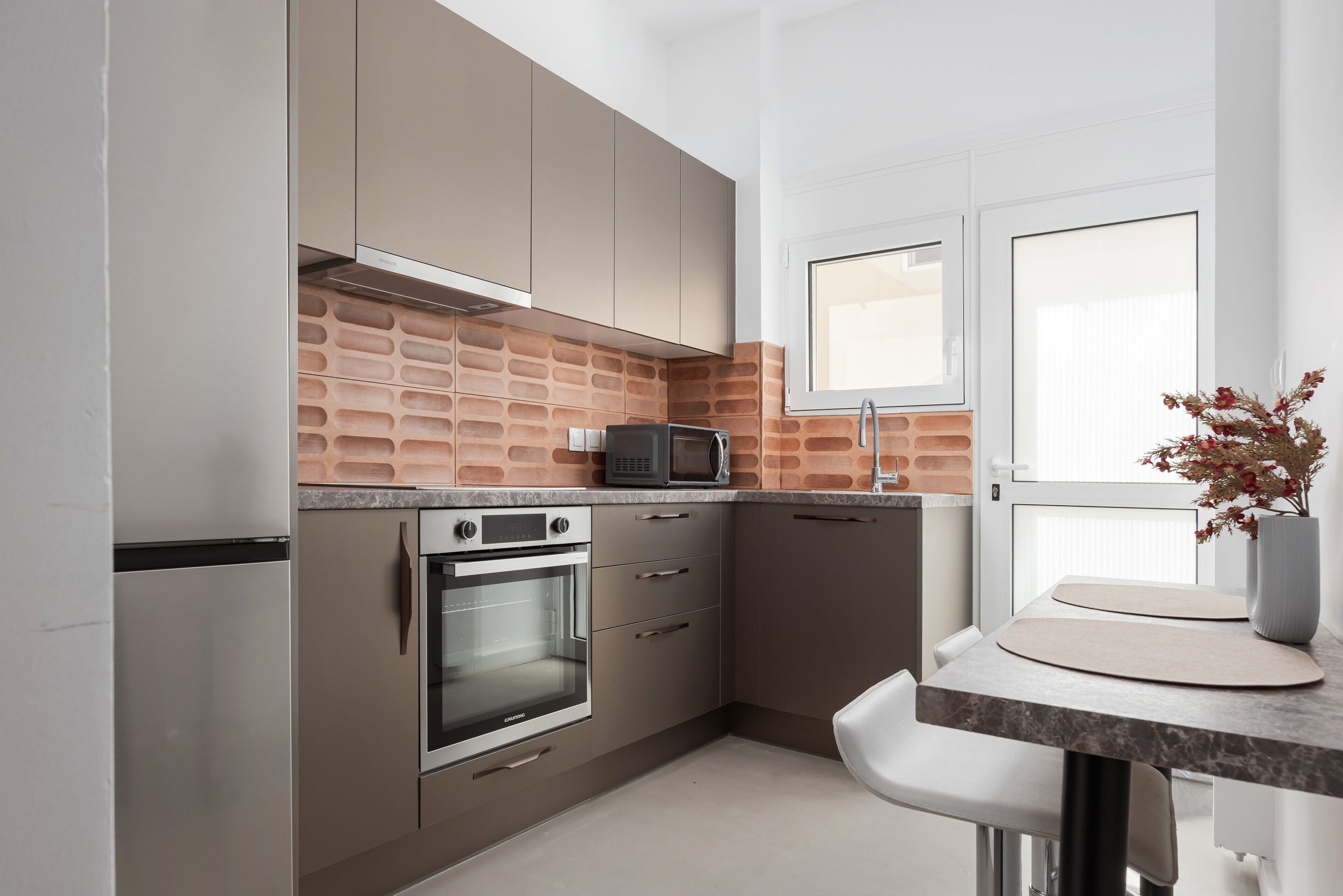 A modern kitchen with stainless steel appliances, a brick backsplash, and a white dining area.