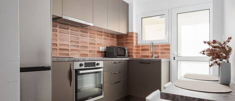 A modern kitchen with stainless steel appliances, a brick backsplash, and a white dining area.