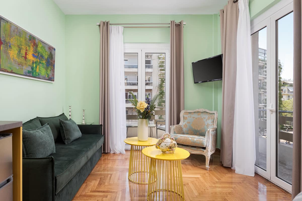 A living room with a green sofa, a yellow coffee table, a decorative chair, and a large window with curtains.