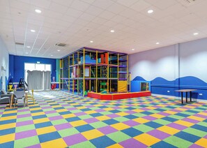 A play area with a colorful checkered floor, a climbing structure, and a view of the sea through a large window.