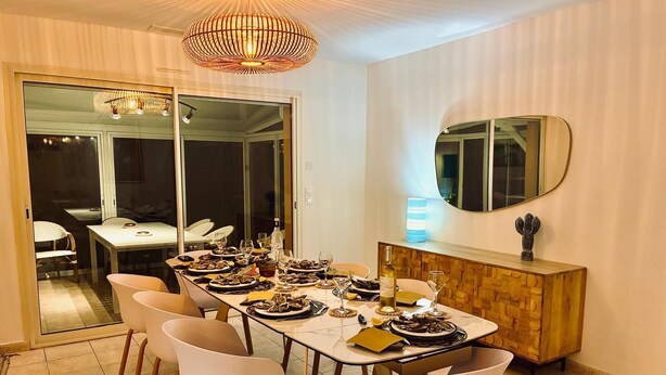 A dining room with a long table set for a meal, chairs, a wooden cabinet, and a large mirror on the wall. - An enchanting haven of calm (Andernos-les-Bains)