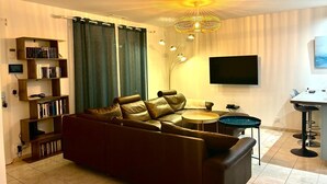 A modern living room with a leather sofa, a bookshelf, a flat-screen TV, and a chandelier. - An enchanting haven of calm (Andernos-les-Bains)