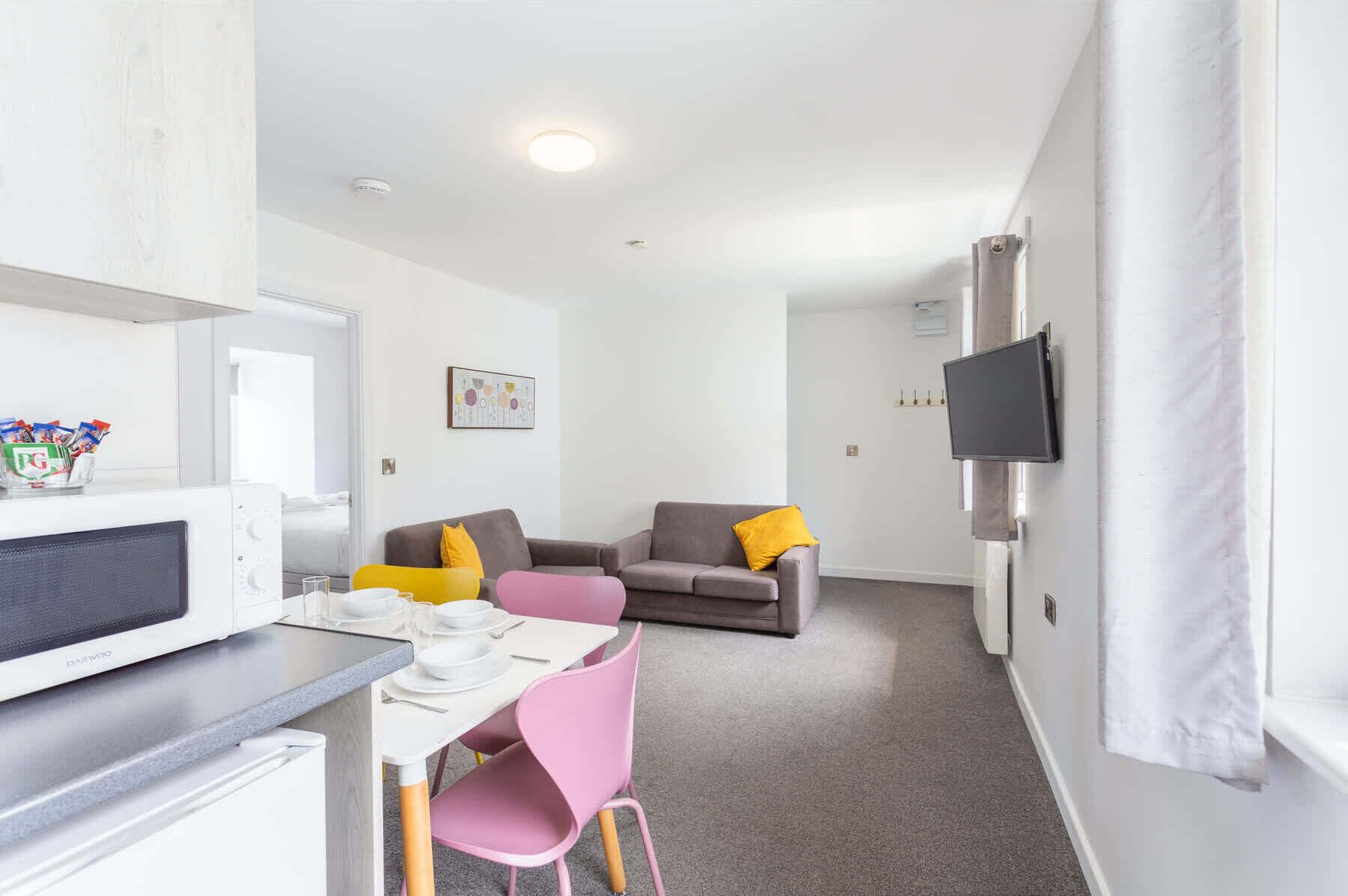 Un espacio habitable compacto con kitchenette, comedor, sofá y televisor montado en la pared.