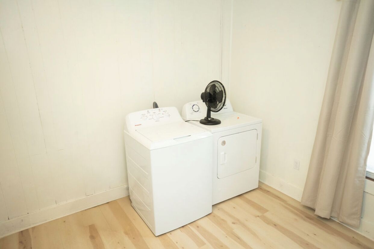 A compact, white laundry room with a washing machine and a fan.