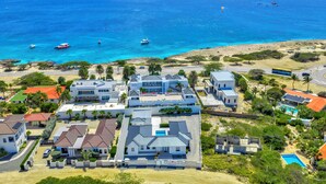 A coastal residential area with houses, a swimming pool, and a view of the ocean. - Malmokweg 4-B (Noord)
