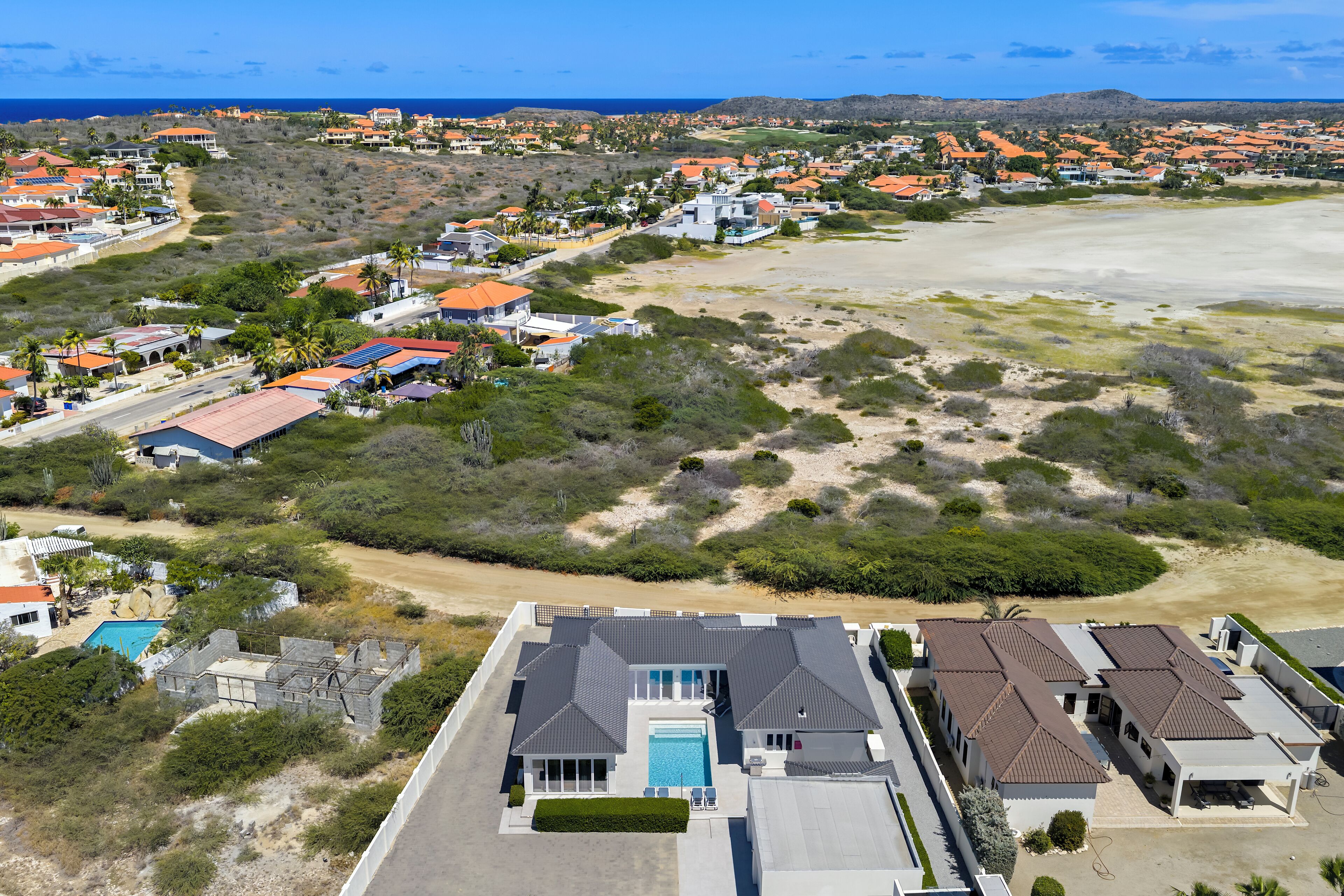 A residential area with houses, a swimming pool, and a beach in the background.