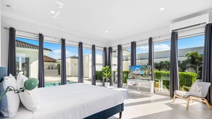 A modern bedroom with a large bed, a view of a swimming pool, and a balcony with a chair. - Malmokweg 4-B (Noord)