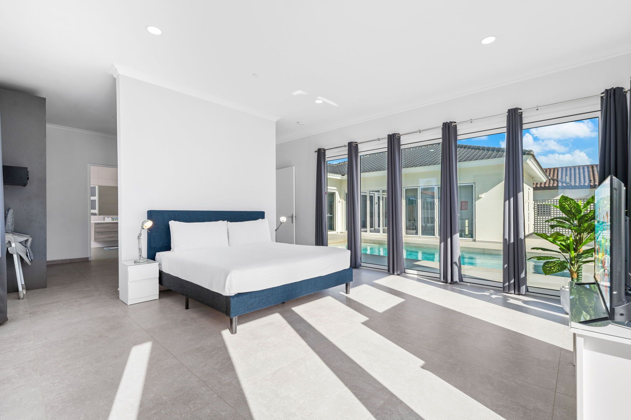 A modern bedroom with a large bed, a bedside table, a nightstand, a desk, and a large window with a view of a swimming pool.